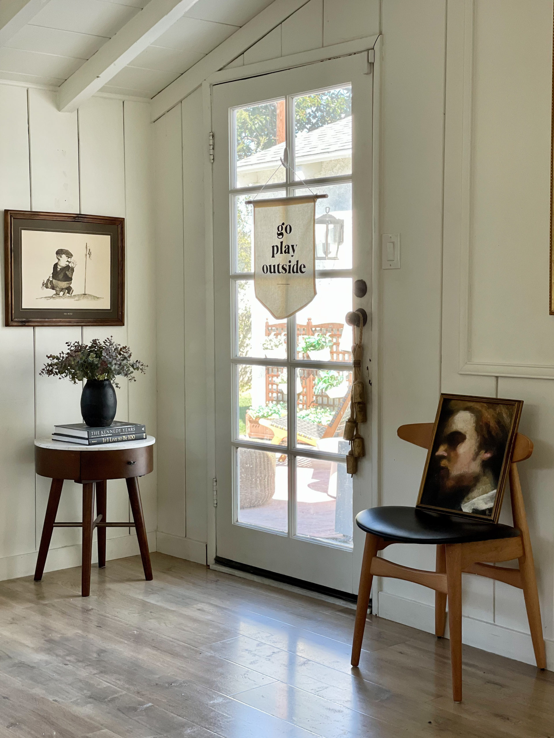 art on chair, art in unexpected places, shiplap wainscoting, swiss coffee walls, modern traditional home, pretty on fridays, back door, glass door, shiplap walls, wooden laminate floors, vaulted ceilings, painted beams, shiplap ceiling, 1950 beach cottage thrifted art, bells on door, side table